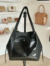 Bolso tote negro de cuero con bolsillo frontal de charol con diseño de piel de cocodrilo.