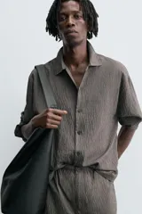 Camisa de corte relajado confeccionada en tejido fluido con mezcla de modal, presenta un diseño de rayas verticales con textura efecto arrugado, cuello solapa, cierre frontal de botones y manga larga con puños abotonados.