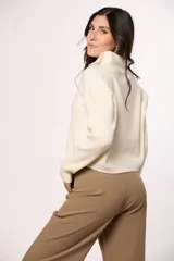 Buzo tejido de punto color beige, con cuello alto y cierre frontal parcial. Presenta mangas largas con diseño en tejido morley y corte holgado.