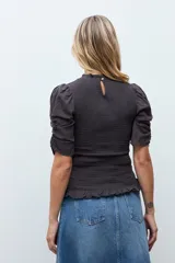 Blusa de color gris oscuro con diseño de punto smock en el cuerpo, cuello redondo y mangas cortas abullonadas con detalle de volados en el ruedo.