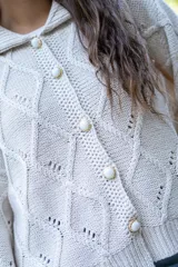 Saco tejido de punto con diseño de ochos y trenzas, color negro. Presenta cuello estilo camisero, cierre frontal con botones tipo joya, mangas holgadas y silueta oversize.