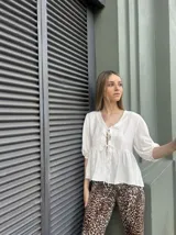 Blusa blanca con escote en V y lazos decorativos, mangas 3/4 abullonadas y corte holgado.