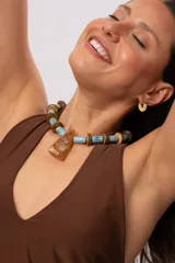 Collar corto con cuentas cilíndricas celestes de cerámica, cuentas circulares de madera y un gran dije colgante de acrílico ambarino en forma de trapecio.