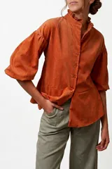 Camisa de pana color naranja, con cuello mao con volados, mangas abullonadas y corte peplum en la cintura. Presenta cierre frontal con botones.