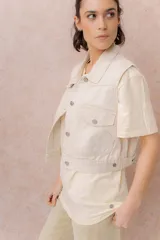 Chaleco de jean color crudo, con calce relajado y largo a la cintura. Cuenta con cuello camisero, cierre frontal con botones metálicos y bolsillos delanteros con tapa.