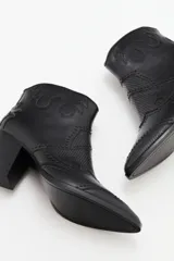 Bota corta estilo western de cuero vacuno negro, con puntera fina y detalles de textura grabada tipo reptil. Presenta costuras decorativas y apliques de tachas metálicas pequeñas en el diseño. Cuenta con taco cuadrado y cierre lateral.