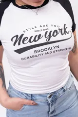 Remera baby tee blanca con mangas cortas raglán negras, corte ajustado al cuerpo y estampado frontal con texto en negro alusivo a New York.
