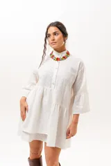 Vestido corto de broderie color crudo, con cuello camisero, cierre frontal parcial con botones, mangas tres cuartos acampanadas y corte evasé con volados.