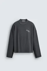 Sudadera de corte relajado confeccionada en tejido de algodón con textura acanalada. Presenta cuello redondo, manga larga y un diseño con efecto lavado. Incluye un texto estampado en contraste en la parte frontal.