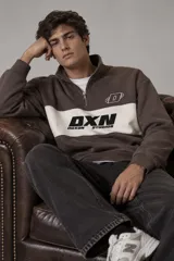 Buzo de cuello alto con medio cierre y diseño en bloques de color marrón y una franja blanca ancha en el pecho. Cuenta con estampado tipográfico de la marca "DXN Duxon Studios" en color negro sobre la franja blanca y un logotipo pequeño en el pecho.