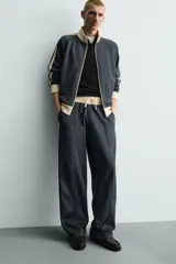 Pantalón jogger de corte wide fit en tejido compacto color gris oscuro. Presenta cintura elástica con cordón ajustable, bandas laterales en contraste color beige y costuras frontales tipo pinza.