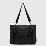 Tote bag color marrón, con diseño minimalista y logo de la marca grabado en el frente. Cuenta con doble asa de mano y una correa larga ajustable y extraíble, ambas con el nombre de la marca estampado. Incluye un bolsillo frontal con cierre.