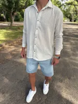 Camisa de lino blanca con rayas verticales beige, de manga larga, cuello camisero y cierre frontal de botones.