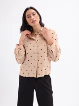 Blusa de algodón color beige con estampado de lunares negros, manga larga abullonada, cuello mao y cierre frontal con botones.