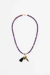 Collar de cuentas de vidrio facetadas en color violeta, con dije central compuesto por una borla negra, un dije de sol con piedra negra y un dije en forma de cuerno.