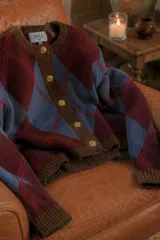 Cardigan de punto con patrón argyle en tonos bordó y rosado, con detalles en verde oscuro en cuello, puños y ruedo. Presenta cierre frontal con botones dorados.