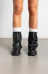 Botas de cuero negro con caña media y diseño holgado con efecto fruncido en la parte superior. Presentan una suela plana con taco bajo y puntera redondeada.