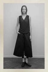 Bermuda sastrera negra unisex de popelina o gabardina de algodón, con pretina elástica, tiro bajo, bolsillos laterales, cierre lateral y pliegue delantero de gran tamaño.