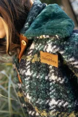 Buzo canguro oversize de paño de lana gris con capucha estampada y cuello de corderito blanco. Cuenta con aberturas laterales en el ruedo y detalles de cuero sintético marrón en el cierre frontal y etiqueta.