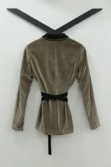 Blazer tipo smoking de terciopelo negro con acabado brillante y detalles estampados en dorado. Presenta solapas clásicas, cierre frontal cruzado mediante un lazo y mangas largas con cierres incorporados. El diseño es entallado y sofisticado.