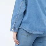 Blusa recta de jean azul claro, con cuello camisero, escote en V con abertura y un bolsillo aplicado en el pecho.