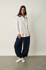Chaleco de punto color beige claro con escote en V, sin mangas y diseño abierto en los laterales con ajuste de cintas para atar.