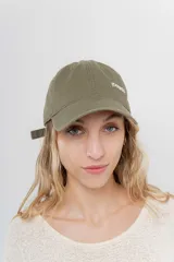 Gorra verde militar de diseño clásico con visera curva y aplique metálico plateado con la inscripción "Peach" en el lateral frontal. Cuenta con tira ajustable en la parte trasera.