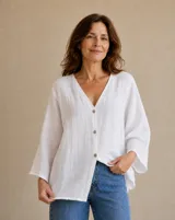 Camisa blanca de lino, con cuello en V, cierre frontal con botones y mangas tres cuartos anchas.