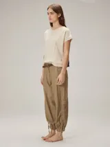 Pantalón de corte relajado color marrón, confeccionado en mezcla de algodón y lino. Presenta cintura con pasacintos, bolsillos laterales y diseño de botamanga ajustable con cordones y elástico.