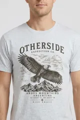 Remera blanca de manga corta y cuello redondo, confeccionada en algodón, con estampa frontal de un águila volando sobre montañas y la inscripción "Otherside Expedition Co. Andes Mountains Argentina".