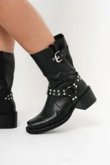 Bota biker de caña media color negro, con hebilla en la parte superior y detalle de aro y tachas en la parte inferior.
