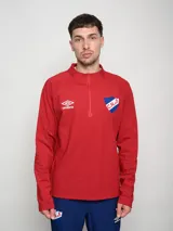 Buzo deportivo de polytraining color rojo, con medio cierre frontal y cuello alto. Presenta el logo de Umbro en el pecho izquierdo y el escudo del Club Nacional de Football en el pecho derecho.
