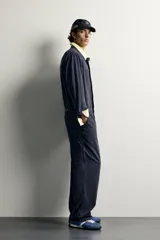 Mono oversize fit de algodón con estructura espiga en color azul marino, con cuello solapa en contraste de color tostado, manga larga, bolsillos de plastrón en el pecho con firma bordada, trabillas laterales en la cintura y cierre frontal con cremallera y botonadura oculta.