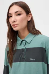 Remera tipo polo de manga larga con diseño de rayas horizontales anchas en bloques de color crema y beige. Presenta cuello camisero con cierre de botones y un pequeño bordado en el pecho.