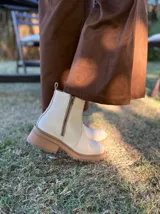 Bota corta de cuero vacuno con textura granulada, color crudo. Presenta cierre lateral metálico, tirador en la parte trasera y suela track de goma en tono contrastante.