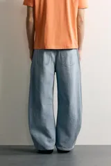 Jeans de denim de algodón color gris con efecto lavado, de corte relaxed barrel fit y tiro medio. Presenta diseño amplio con pinzas en las rodillas y costuras curvas, cierre frontal con botones y cinco bolsillos tradicionales.