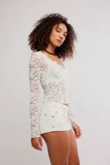 Remera de encaje floral blanca de manga larga y calce ajustado, con escote en V y diseño semitransparente.