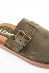 Zueco de gamuza color verde oliva, con diseño cerrado en la parte frontal y hebilla metálica dorada ajustable en el empeine. Presenta una suela de goma dentada en color marrón.