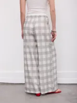 Pantalón de corte ancho y fluido, con estampado a cuadros en tonos grises y blancos, cintura alta con trabillas y bolsillos laterales.