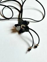 Gargantilla negra con dije de flor con detalles brillantes y cordón ajustable.