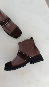 Botín de cuero marrón con paneles de gamuza en puntera y empeine, decorado con tachas metálicas plateadas y suela track negra.