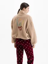 Campera de tejido polar color beige con cuello alto, cierre frontal y bolsillos laterales con cierre. Presenta bordado 'APRÈS SKI' en el pecho y detalles en color tostado en los bordes. Diseño de corte holgado con mangas largas.