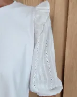 Remera blanca de algodón con cuello redondo, mangas tres cuartos abullonadas y detalle de volados en los hombros.