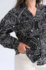 Blusa de manga larga con cuello mao y cierre frontal de botones. Presenta un diseño estampado con líneas blancas abstractas sobre fondo negro.
