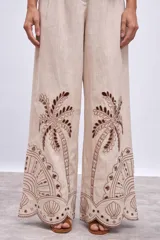 Pantalón de lino color beige con bordados de palmeras y conchas marinas en color marrón.