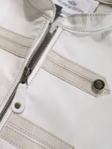 Chaqueta color beige con cierre frontal y detalles de tiras horizontales en el frente y hombros con botones metálicos.