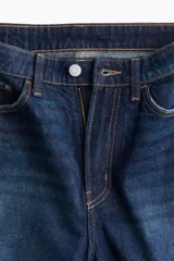Pantalón de jean azul oscuro, de tiro alto, corte recto y pierna ancha. Diseñado para siluetas con curvas, ceñido en la cintura y holgado en cadera y muslos. Confeccionado en denim de algodón rígido y cuenta con cinco bolsillos.
