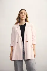 Blazer de mujer color rosa pálido, de corte recto y largo, con solapas de muesca y un solo botón frontal marrón. Presenta bolsillos de parche en la parte delantera y mangas tres cuartos.