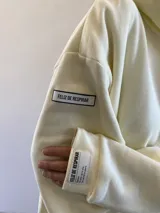 Hoodie oversize color beige con capucha y cordones ajustables. Presenta un pequeño logo bordado de un león con corona en el pecho y un bolsillo frontal tipo canguro.