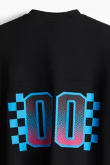 Remera de malla negra con cuello en V, mangas cortas y hombros caídos. Presenta un estampado frontal con la frase "THUNDER X RACING TEAM" y un diseño gráfico en tonos rosa, azul y celeste con la palabra "RACING" y un patrón de cuadros.